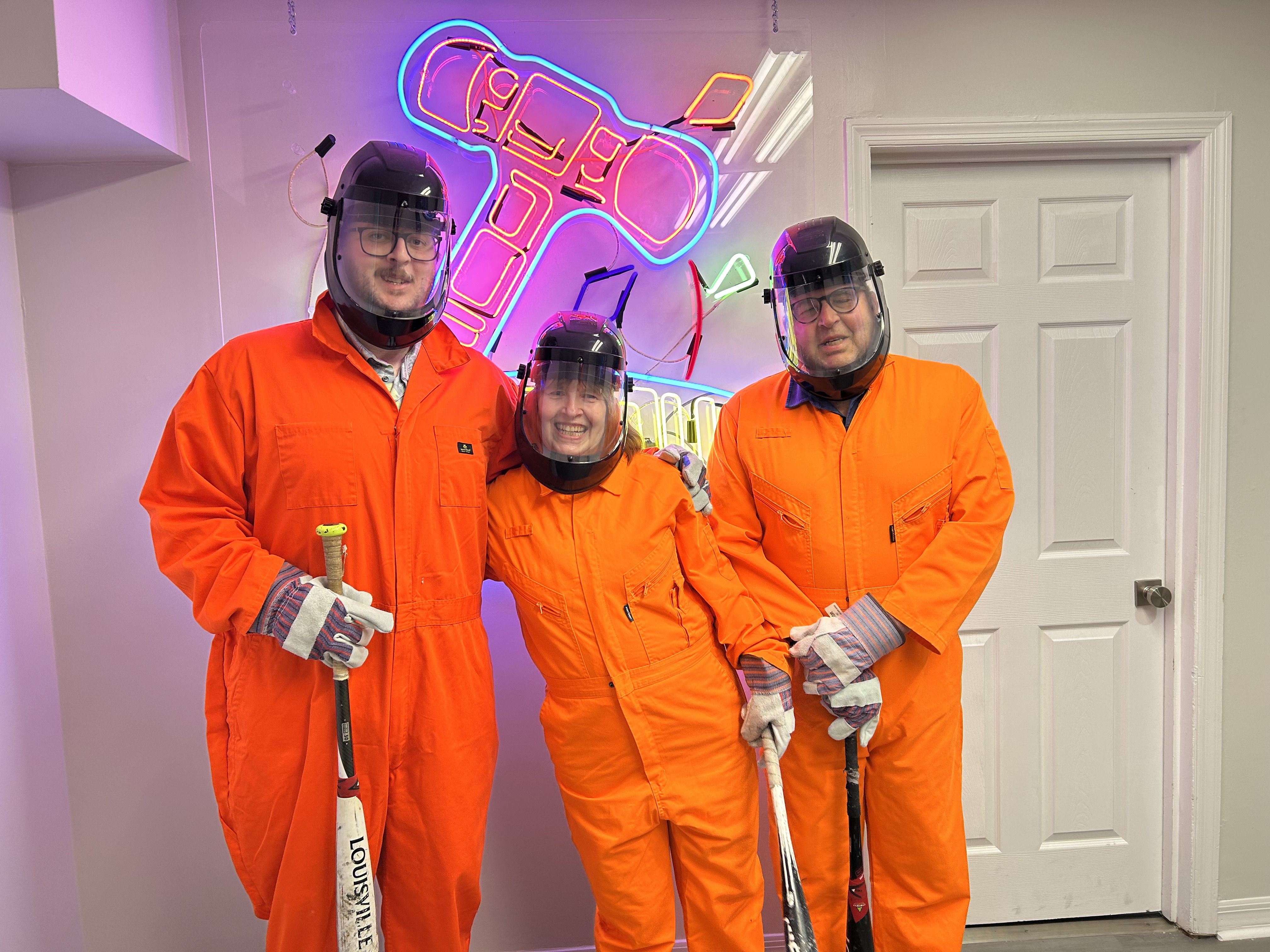Three Crash Out customers in orange jumpsuits smiling and ready to smash
