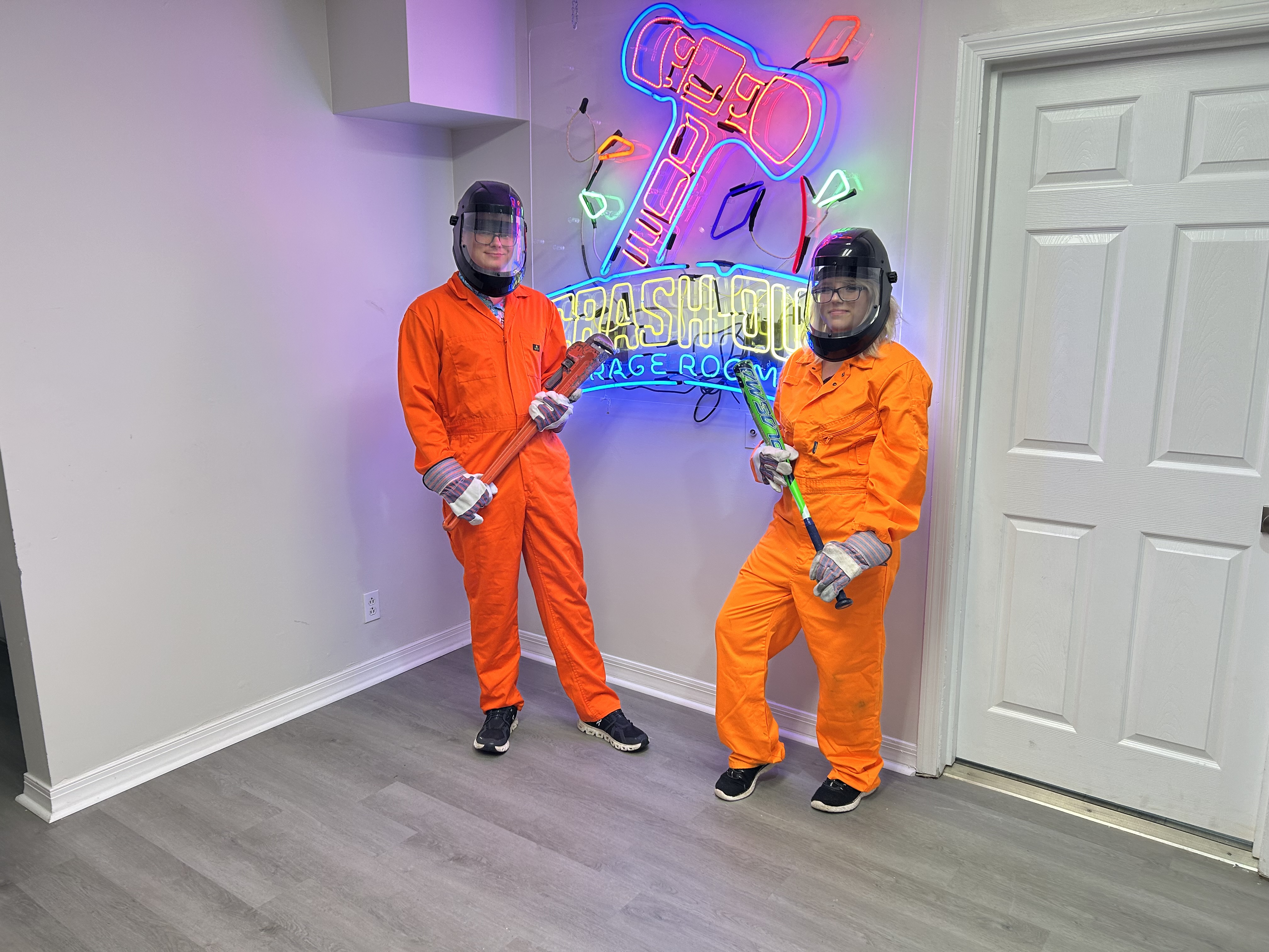 Large group of Crash Out customers in orange jumpsuits holding bats in front of branded neon sign